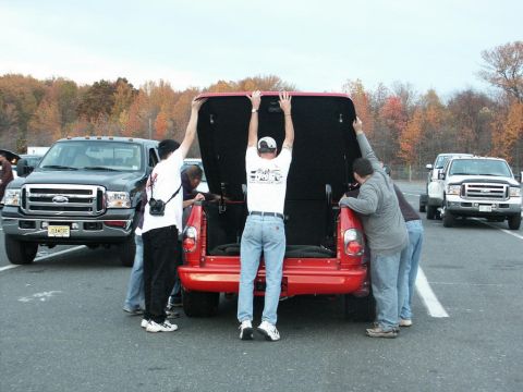 2001 Mercury Grand Marquis - People work on the bed of a red pickup truck while other Ford trucks are parked nearby.