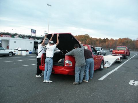 2001 Mercury Grand Marquis - People are working on the bed of a red pickup truck at what appears to be a race track.