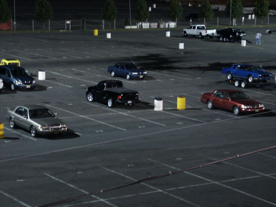 Cars parked in a lot at night, some are trucks and sedans