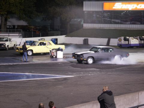 2001 Mercury Grand Marquis - Two cars are on a drag strip, one performing a burnout with smoke billowing from its tires.