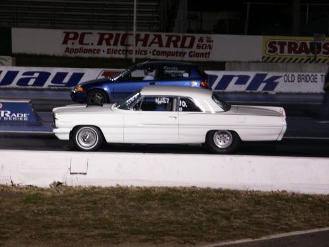 2001 Mercury Grand Marquis - A white classic coupe races a blue hatchback on a drag strip, with various sponsor banners visible in the background.