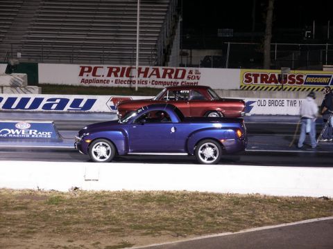 2001 Mercury Grand Marquis - Two vehicles race down a drag strip at night, with spectators and advertising in the background.
