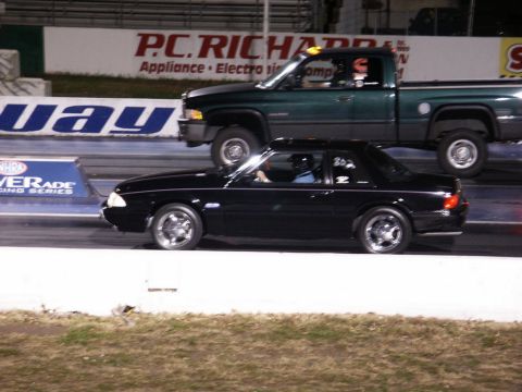 2001 Mercury Grand Marquis - A black coupe races a green pickup truck down a drag strip.