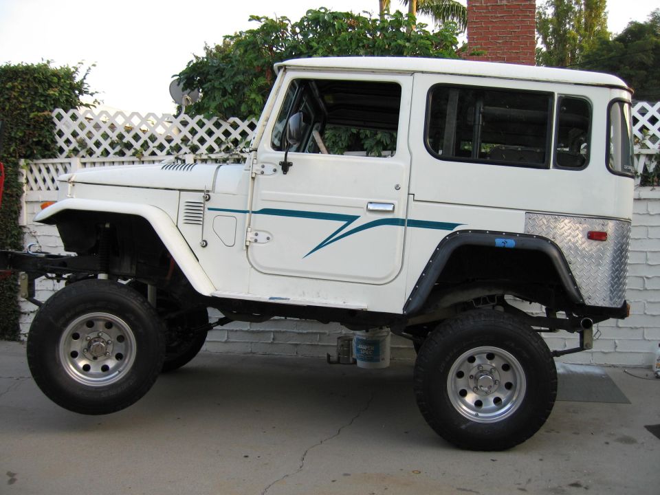 White 1977 Toyota Land Cruiser FJ40 with teal stripe on door, diamond plate rear quarter panel, and lifted suspension