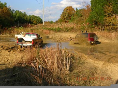 1989 Ford Bronco II - Multiple off-road vehicles navigate a challenging muddy terrain under a partly cloudy sky.