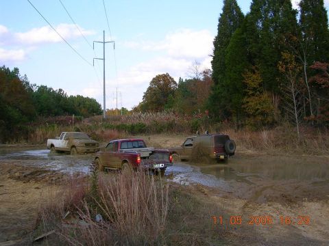 1989 Ford Bronco II - Multiple trucks navigate a muddy off-road course under a cloudy sky.