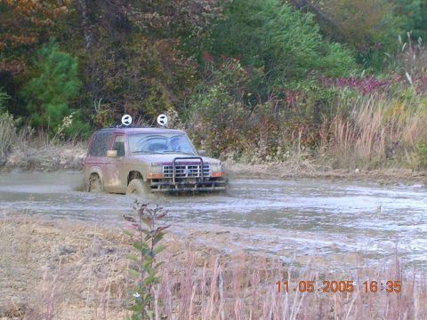 1989 Ford Bronco II - A 1989 Ford Bronco II is stuck in a muddy area, with trees and vegetation surrounding it.