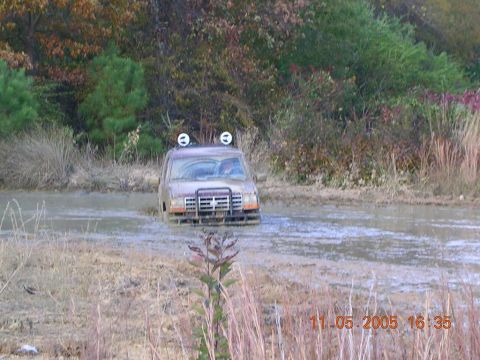1989 Ford Bronco II - A 1989 Ford Bronco II navigates through a muddy terrain, its front end submerged in water.