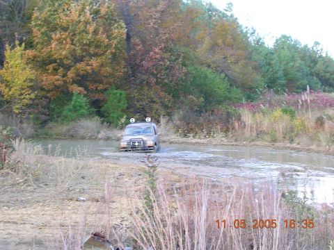 1989 Ford Bronco II - A tan SUV navigates a muddy terrain, its front grille and roof lights visible.