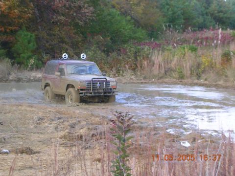 1989 Ford Bronco II - A 1989 Ford Bronco II navigates through a muddy terrain, kicking up water as it goes.