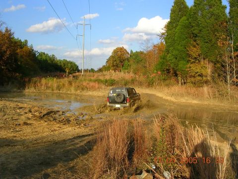 1989 Ford Bronco II - A dark SUV navigates a muddy track, kicking up water and dirt.