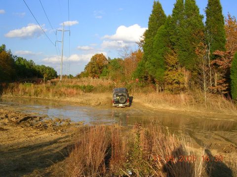 1989 Ford Bronco II - A 1989 Ford Bronco II navigates a muddy off-road course on a clear day.