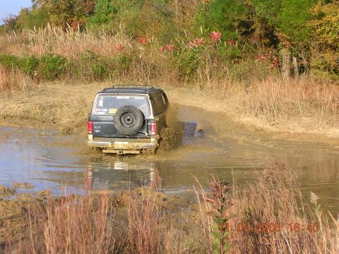 1989 Ford Bronco II - A 1989 Ford Bronco II navigates a muddy off-road trail, kicking up water and mud.