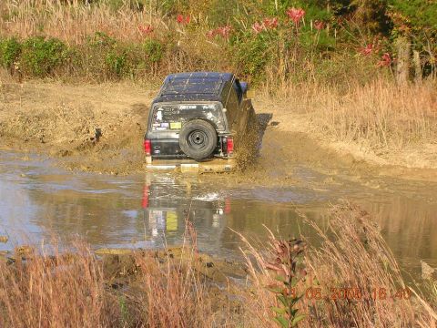 1989 Ford Bronco II - A black 1989 Ford Bronco II navigates a muddy trail, kicking up water and dirt.