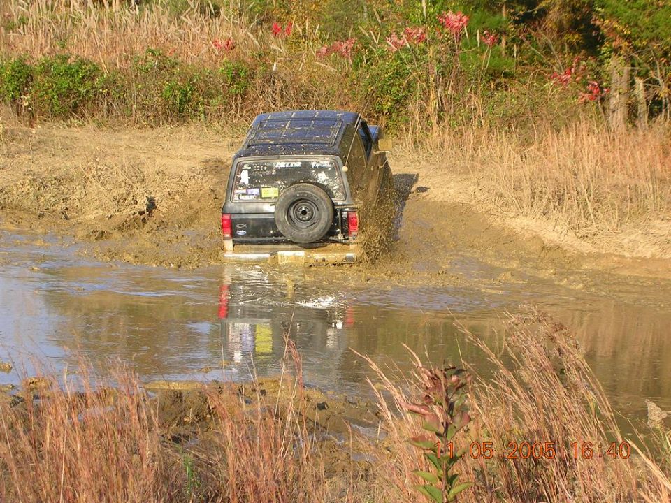 Black 1989 Ford Bronco II driving through mud, rear view, spare tire mounted on back