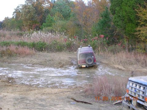 1989 Ford Bronco II - A maroon 1989 Ford Bronco II is stuck in a muddy ditch, with part of another vehicle visible.