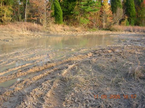 1989 Ford Bronco II - A muddy landscape with visible tire tracks and a water puddle, suggesting off-road activity.