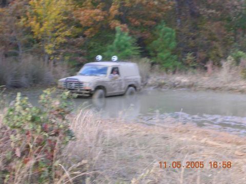 1989 Ford Bronco II - A 1989 Ford Bronco II navigates a muddy trail, its front end partially submerged in water.
