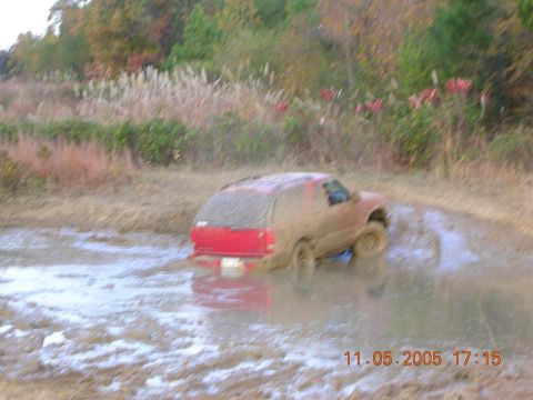 1989 Ford Bronco II - A red SUV navigates a muddy off-road course, kicking up water and mud.