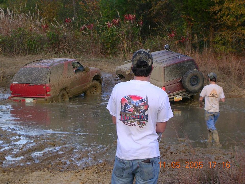 Two off-road vehicles stuck in deep mud with people watching