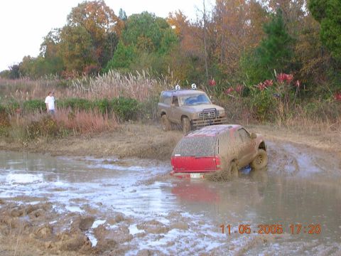 1989 Ford Bronco II - Two SUVs navigate a muddy terrain, with one deeply stuck in the mire.