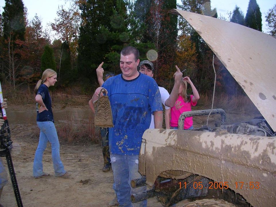 Mud-covered 1989 Ford Bronco II with hood open, front view. People stand around it