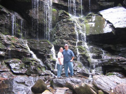 1985 Ford LTD Crown Victoria - A couple stands on rocks before a cascading waterfall.