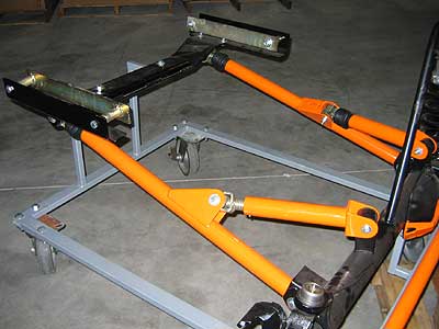 1991 Ford Explorer - Orange powder-coated tubular radius arms and suspension links mounted to a gray steel jig or frame fixture in a shop, with black shock or c…
