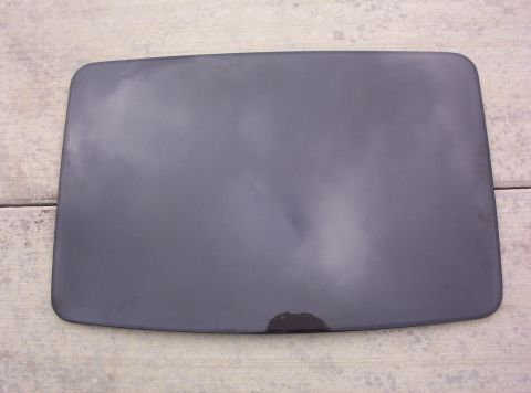 1994 Ford Probe - A dark gray car part, possibly a fuel door, rests on a weathered wooden surface, showing a small stain.