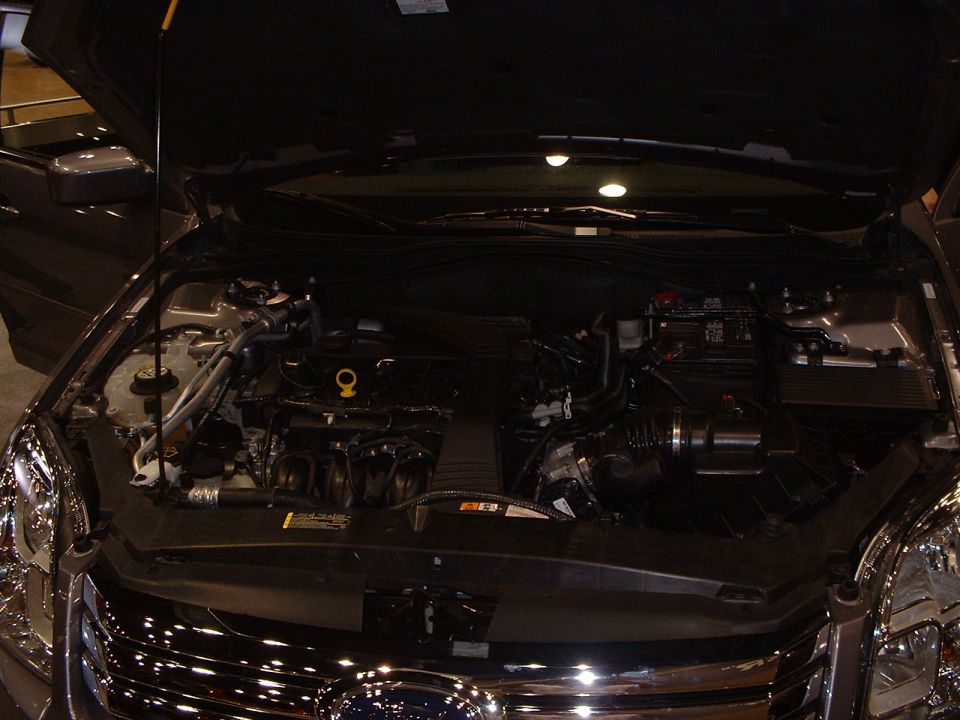 Engine bay of a car with hood open. Shows engine components, battery, and wiring