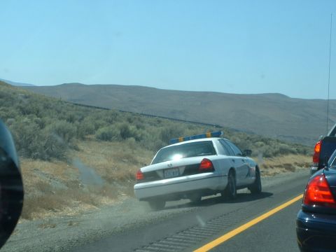 1999 Ford Crown Victoria - A white police car drives on the highway, with a mountainous landscape in the background.