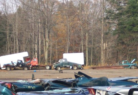 1978 Ford Bronco - A collection of vehicles and trailers sit in a lot, with trees and debris visible.