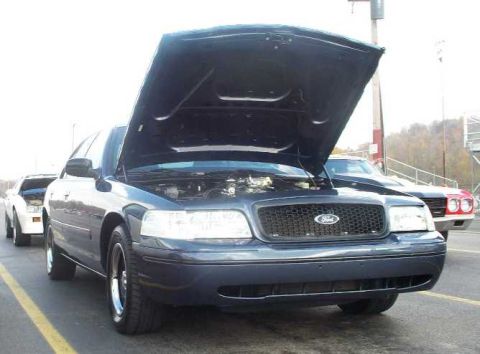 1998 Ford Crown Victoria - A dark blue 1998 Ford Crown Victoria is parked with its hood open, showing the engine bay, alongside other vehicles.