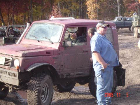 2005 Dodge 1500 - A group of people are gathered around a maroon Suzuki Samurai during an off-road event.