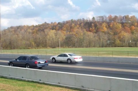 1998 Ford Crown Victoria - Two cars race down a track with autumn foliage in the background.