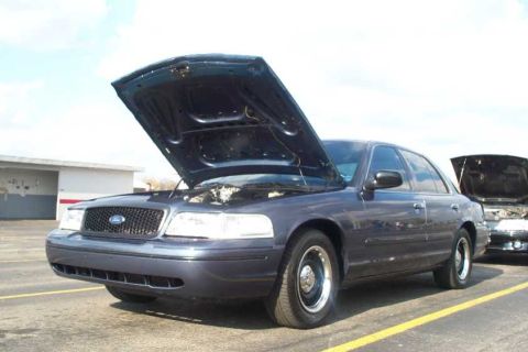 1998 Ford Crown Victoria - A dark blue 1998 Ford Crown Victoria is parked with its hood open, alongside another vehicle with its hood also open.