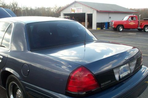 1998 Ford Crown Victoria - A dark blue sedan is parked in front of a building with a red pickup truck visible in the background.