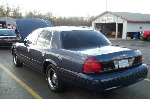 1998 Ford Crown Victoria - A blue 1998 Ford Crown Victoria is parked at an outdoor event with its hood up.