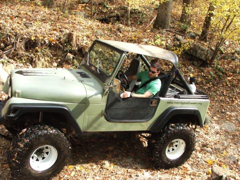 1996 Ford Bronco - A man drives a green Jeep CJ-7 on a wooded trail during autumn.