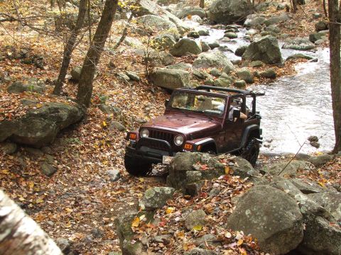 1996 Ford Bronco - Jeep Wrangler TJ driving off-road through a stream during autumn.