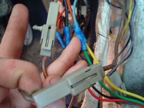 1984 Ford Bronco - A hand manipulates a complex wiring harness with multiple connectors and exposed wires.