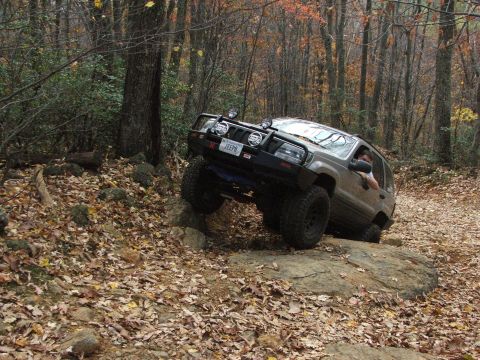 1996 Ford Bronco - A Jeep Grand Cherokee navigates a challenging off-road course in a wooded area during autumn.