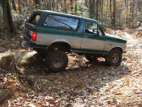 1996 Ford Bronco - This Ford Bronco is navigating a wooded trail with fallen leaves on the ground.