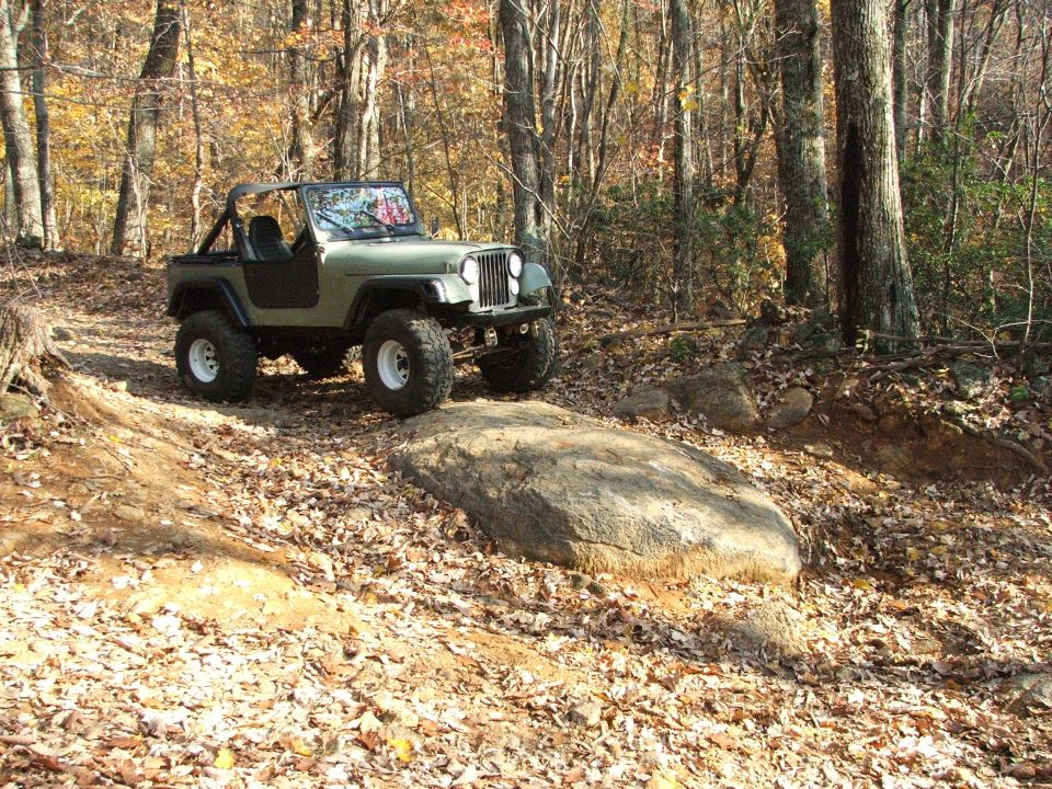Green Jeep Wrangler on a rocky, wooded trail in autumn