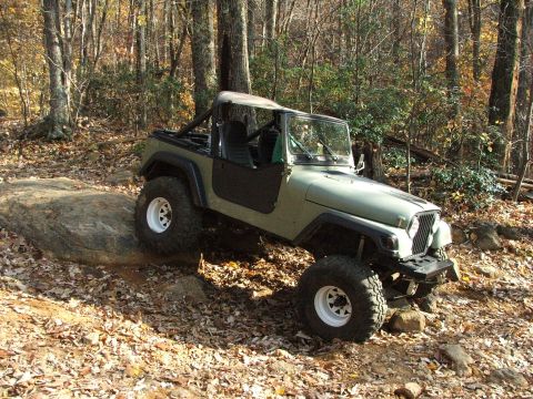 1996 Ford Bronco - This olive green Jeep CJ-7 is shown off-roading on a rocky trail surrounded by autumn foliage.