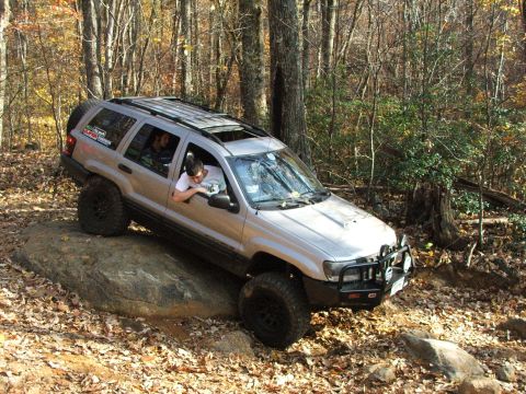 1996 Ford Bronco - A silver Jeep Grand Cherokee navigates a rocky trail in a forest during autumn.