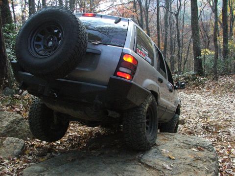 1996 Ford Bronco - Jeep Grand Cherokee navigates a rocky trail in a forest during autumn.