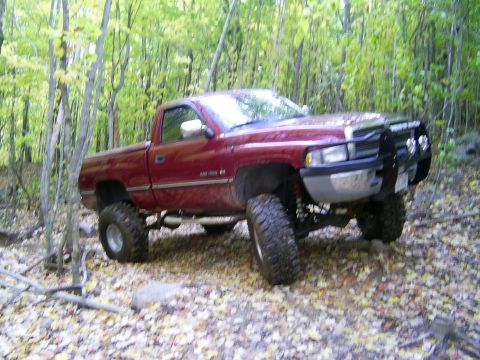 1977 Ford F-150 - A lifted red pickup truck navigates a wooded trail covered in fallen autumn leaves.