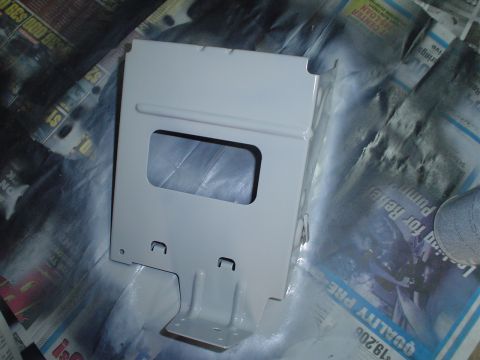 1984 Ford Bronco - A metal bracket is being spray-painted white, with newspaper covering the surface beneath it.