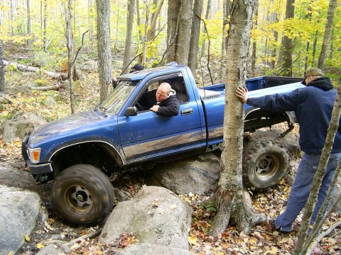 1977 Ford F-150 - A blue pickup truck is being guided through a difficult off-road course by two individuals.